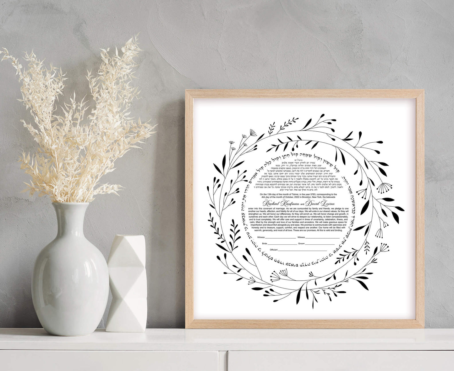 Minimalist floral laurel ketubah displayed in a wooden frame on a shelf.
